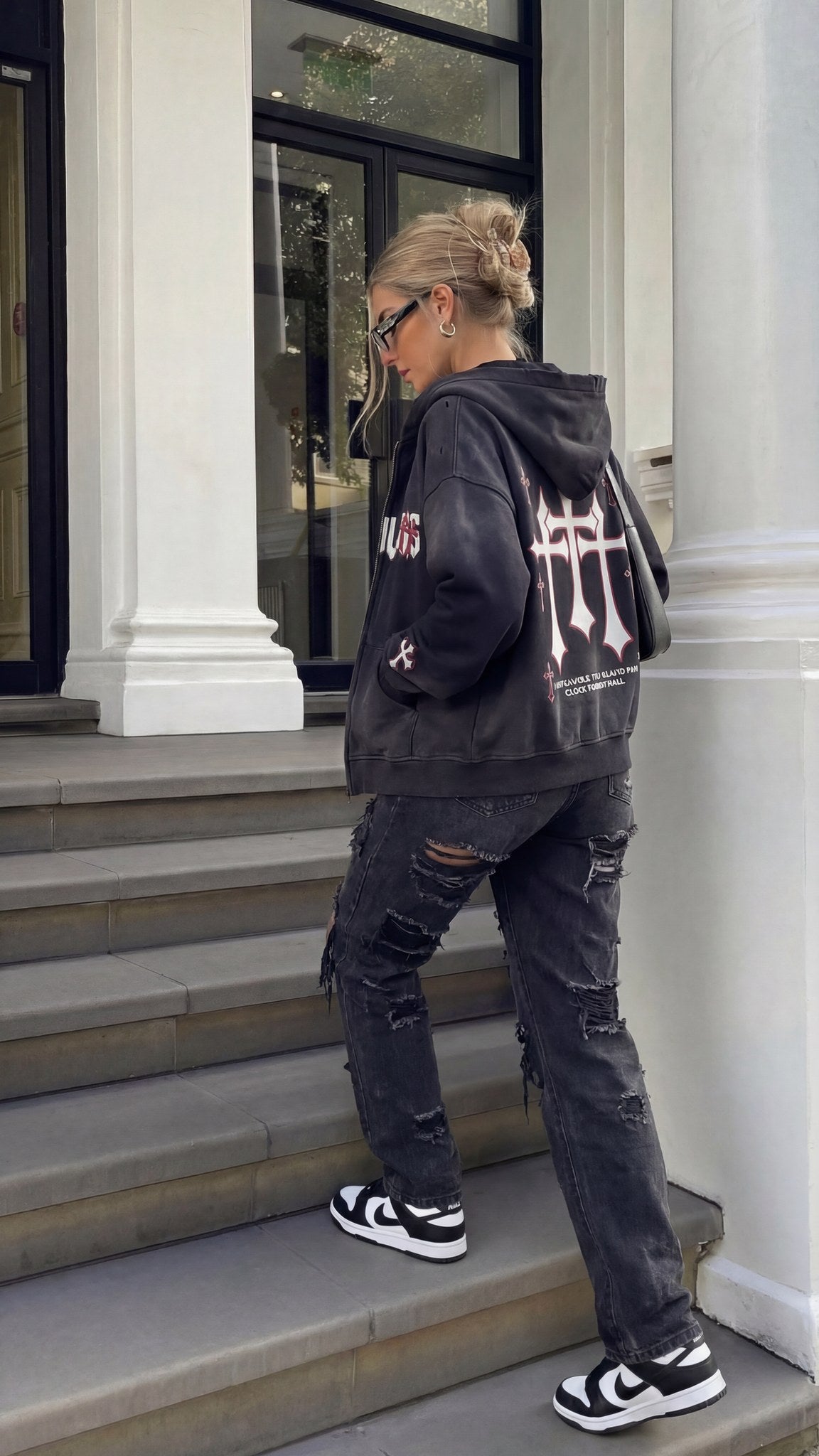 Woman wearing the oversized Saint Villains Redemption black zip hoodie with distressed black jeans, red and white back crosses graphic visible