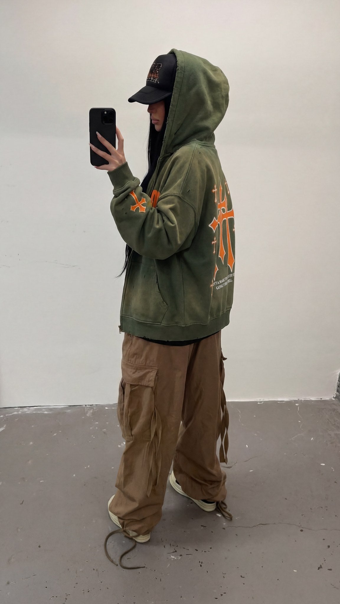 Side view of the Saint Villains Redemption olive green zip hoodie worn with the hood up, orange crosses graphic on the back
